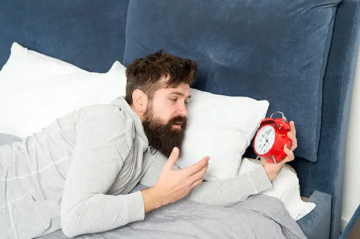 Hombre con barba gruesa mirando un reloj despertador